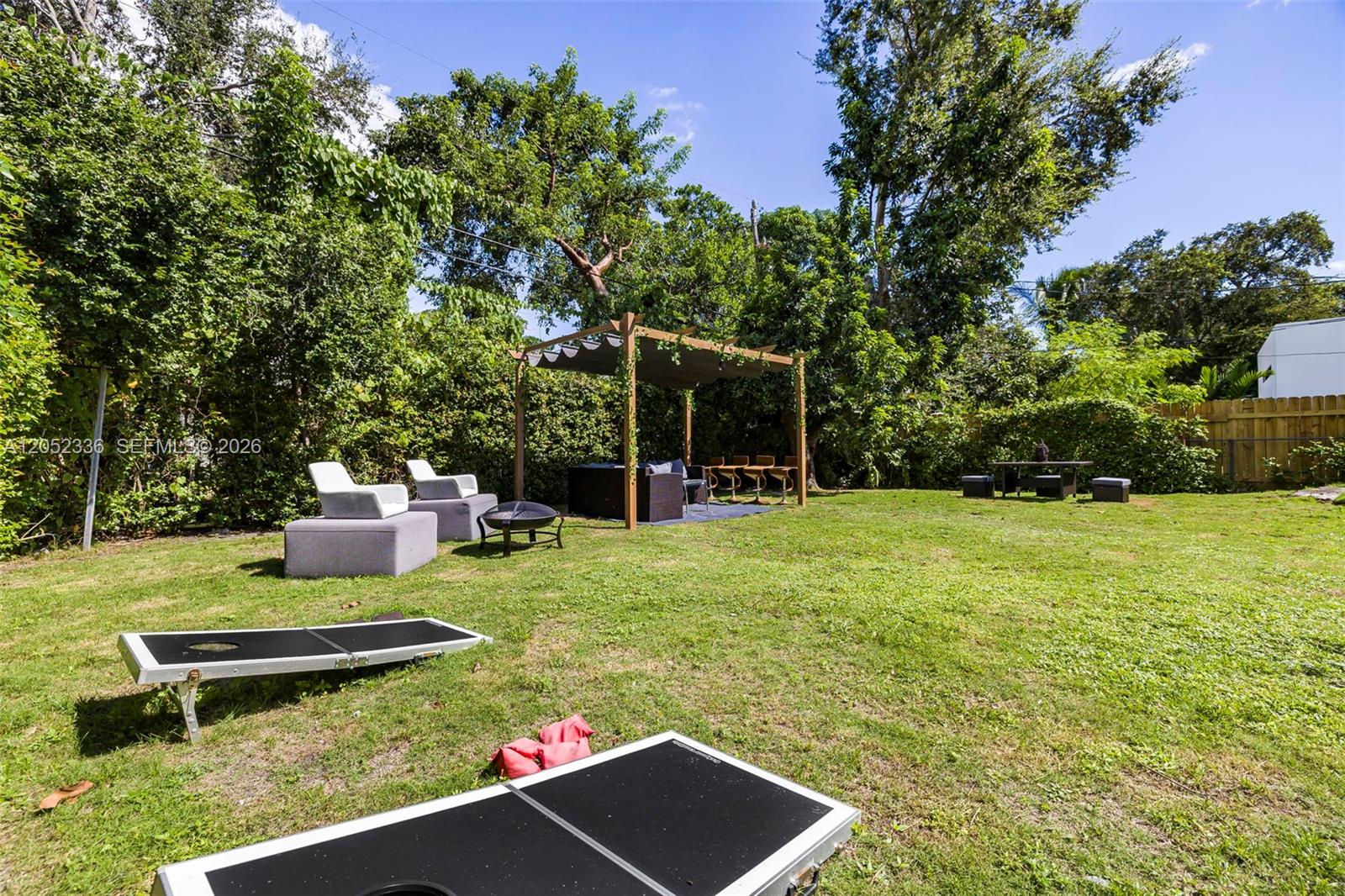 A grassy backyard features a wooden pergola, outdoor seating, and a cornhole game set — 285 NW 45th St # 0, Miami FL 33127, MIAMI, FL