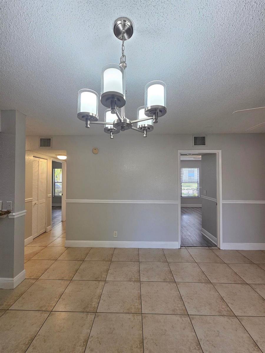 A dining area features a modern chandelier, light gray walls with white wainscoting, and tile flooring — 1700 Windorah Way # A, West Palm Beach FL 33411, WEST PALM BEACH, FL