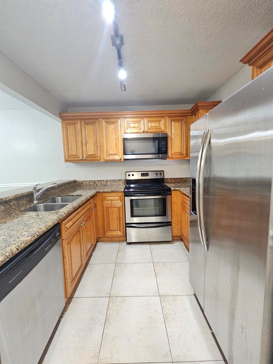 A kitchen features wood cabinets, granite countertops, stainless steel appliances, and light-colored tile flooring — 1700 Windorah Way # A, West Palm Beach FL 33411, WEST PALM BEACH, FL