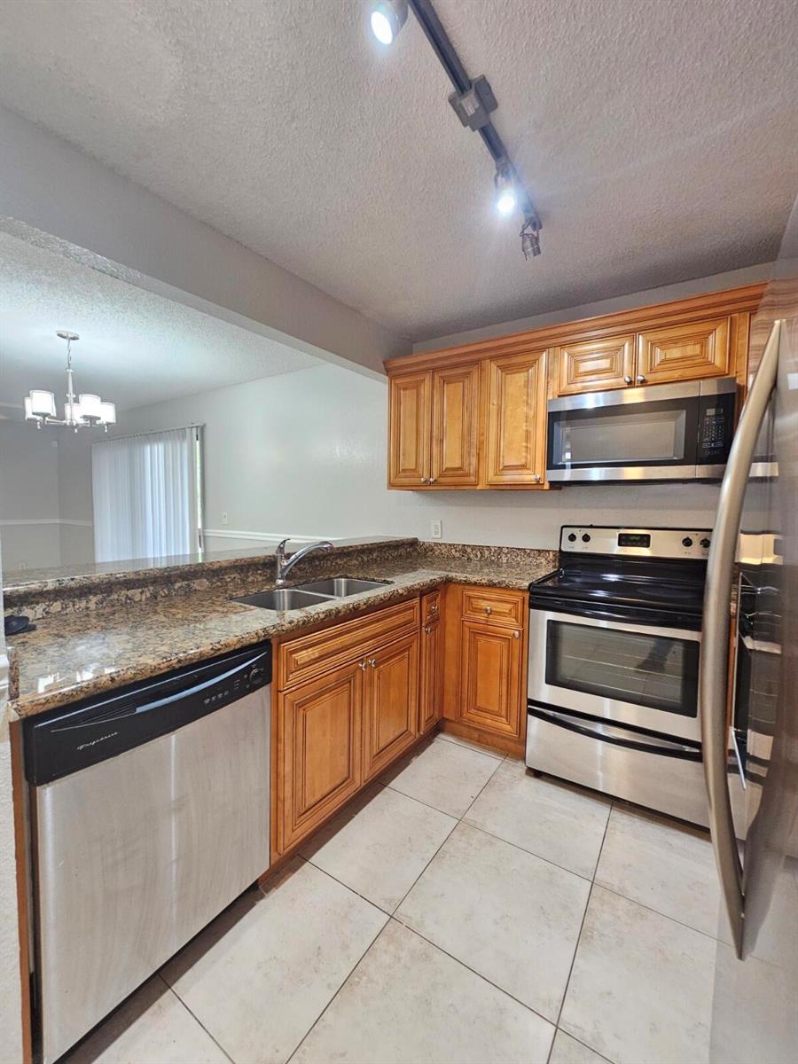 A kitchen features wood cabinets, stainless steel appliances, granite countertops, and light-colored tile flooring — 1700 Windorah Way # A, West Palm Beach FL 33411, WEST PALM BEACH, FL