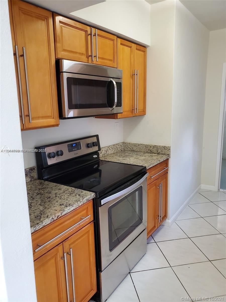 A kitchen features wooden cabinets, stainless steel appliances, and granite countertops over a tiled floor — 1630 NE 157th, North Miami Beach FL 33162, NORTH MIAMI BEACH, FL