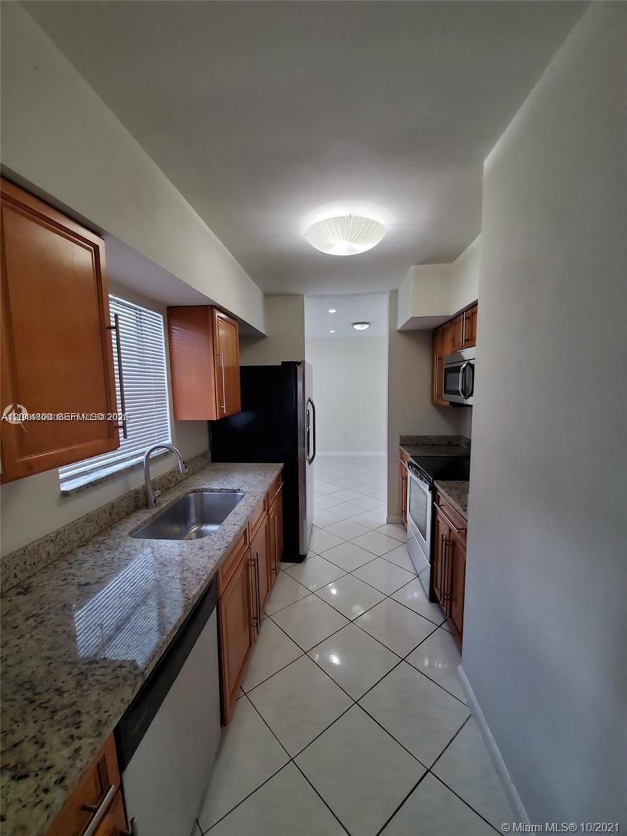 A galley kitchen features wood cabinets, granite countertops, stainless steel appliances, and white tile flooring — 1630 NE 157th, North Miami Beach FL 33162, NORTH MIAMI BEACH, FL