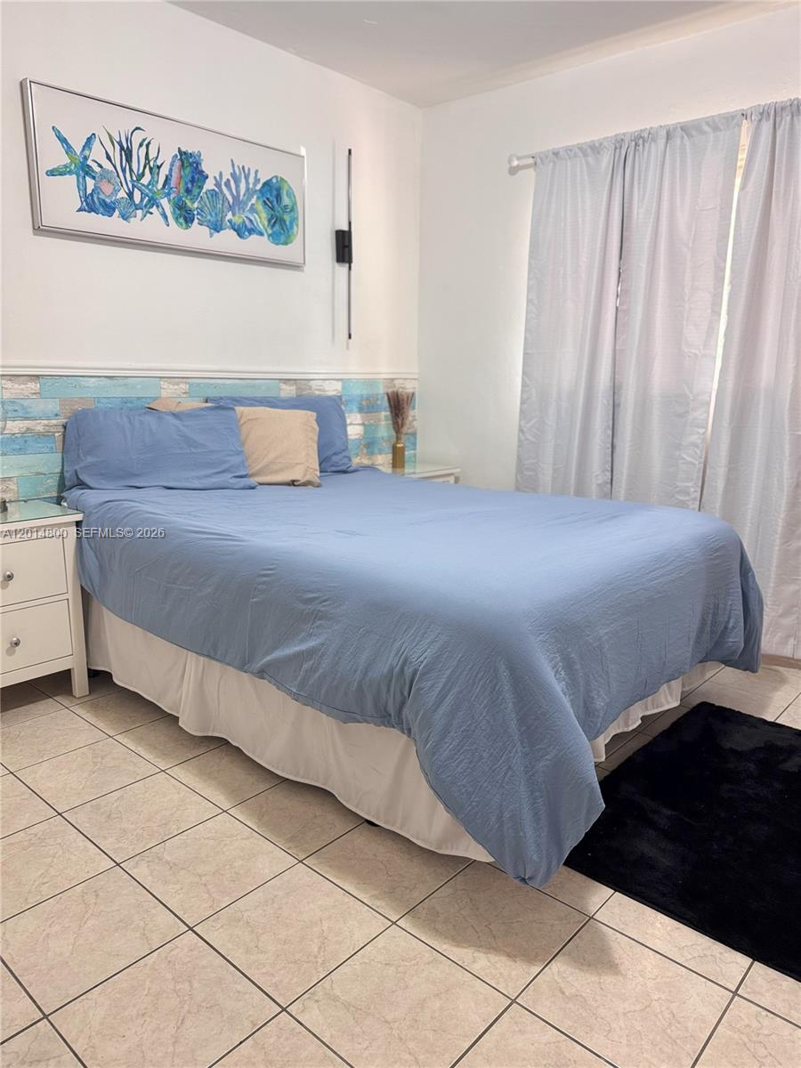 A bedroom features a blue bed, tiled floors, and a coastal-themed wall art piece — 1630 NE 157th, North Miami Beach FL 33162, NORTH MIAMI BEACH, FL