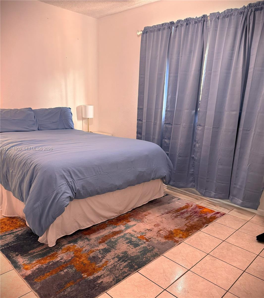 A bedroom features a bed with blue bedding, a patterned area rug, and blue curtains — 1630 NE 157th, North Miami Beach FL 33162, NORTH MIAMI BEACH, FL