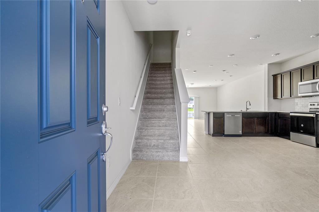 An open-concept interior features a blue front door, carpeted stairs, and a modern kitchen — 2609 BRIGHT JEWEL STREET UNIT 2909, KISSIMMEE, FL
