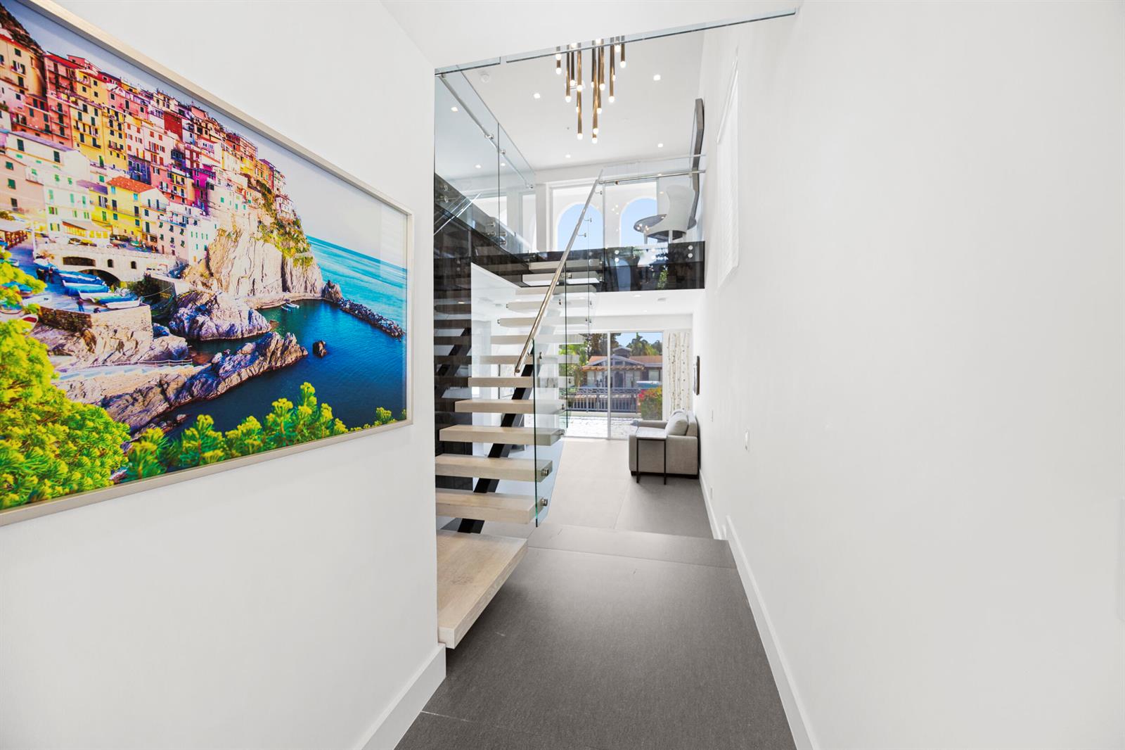 A modern hallway features a floating staircase, glass railings, and a large coastal wall print — 3055 Waterside Circle, Boynton Beach FL 33435, BOYNTON BEACH, FL
