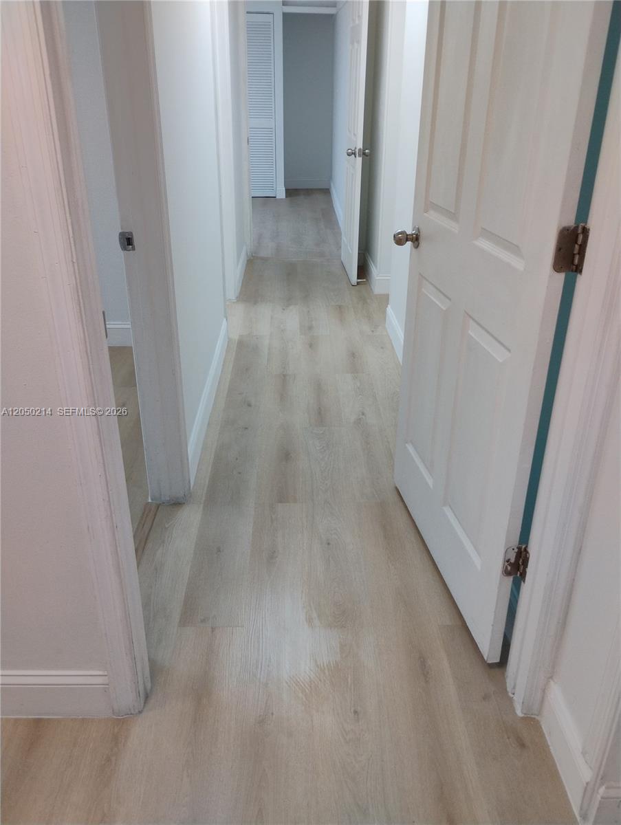 A hallway with light wood-look flooring leads to a doorway with louvered closet doors — 285 NW 27th Ave # 9, Miami FL 33125, MIAMI, FL
