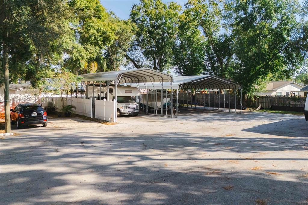 A gravel lot features two metal carports sheltering a motorhome and a boat — 15509 CASEY ROAD, TAMPA, FL