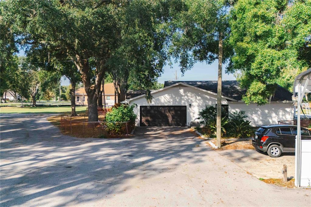 A white house with a dark garage door sits behind a large tree and driveway — 15509 CASEY ROAD, TAMPA, FL