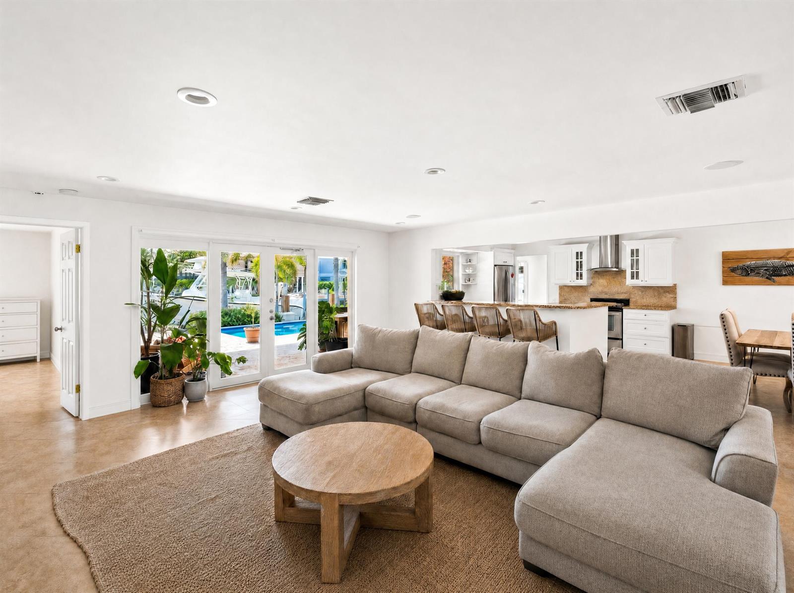 A living room with a large sectional sofa, round wooden coffee table, and kitchen view — 330 SE 10th Street, Pompano Beach FL 33060, POMPANO BEACH, FL