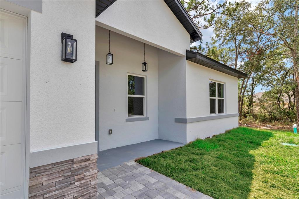 A white stucco house exterior features a stone base, a paved walkway, and hanging lights — 7243 N EMBASSY TERRACE, CITRUS SPRINGS, FL