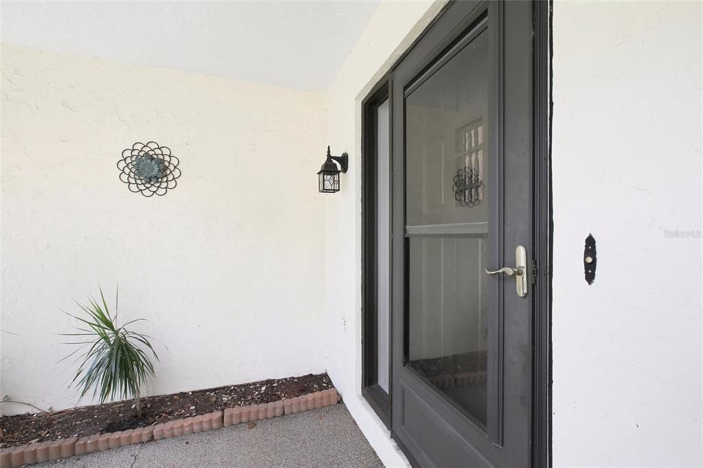 A front entryway features a dark storm door, a wall-mounted lantern, and a small plant — 6947 WOODWIND DRIVE UNIT 77, SARASOTA, FL