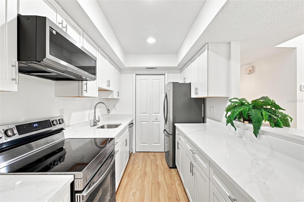 A galley kitchen features white cabinets, quartz countertops, stainless steel appliances, and light wood flooring — 6947 WOODWIND DRIVE UNIT 77, SARASOTA, FL