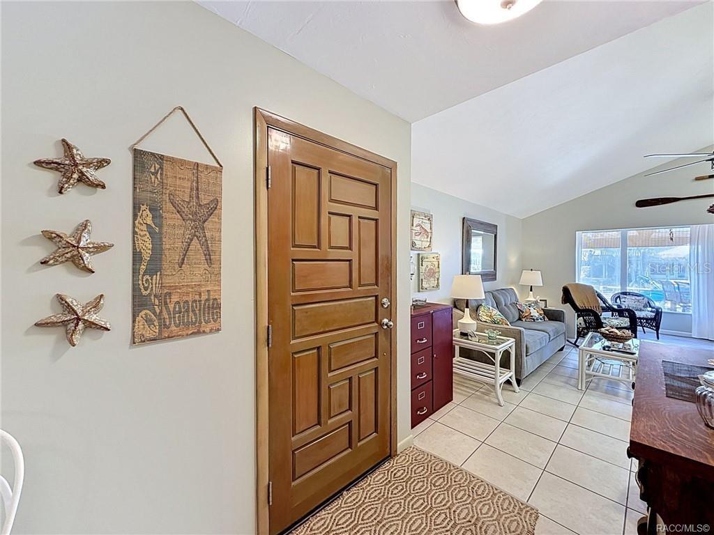 An entryway with a wooden door, tiled floors, and coastal-themed wall decor leads into a living room — 5198 S RIVERVIEW CIRCLE, HOMOSASSA, FL