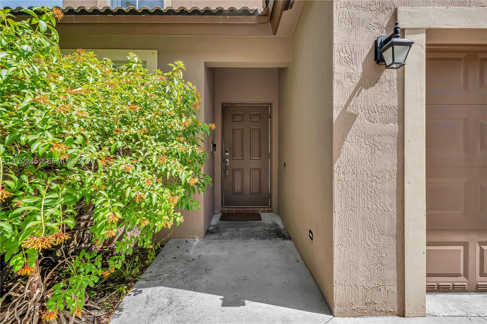 A brown front door is recessed into a beige stucco exterior next to a bush — 2019 SE 13th St, Homestead FL 33035, HOMESTEAD, FL