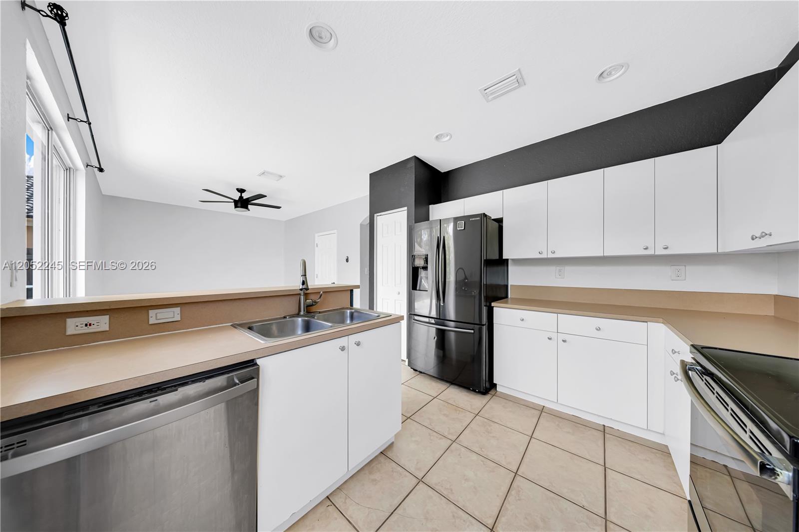 A kitchen features white cabinets, tan countertops, a stainless steel dishwasher, and a black refrigerator — 2019 SE 13th St, Homestead FL 33035, HOMESTEAD, FL