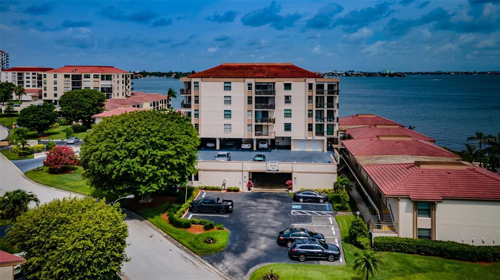 An aerial view shows a multi-story apartment building with a parking lot and waterfront access — 6145 SUN BOULEVARD UNIT 607, ST PETERSBURG, FL