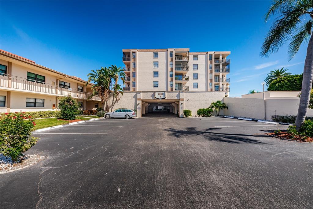 A multi-story apartment building with a ground-level parking garage sits behind an asphalt parking lot — 6145 SUN BOULEVARD UNIT 607, ST PETERSBURG, FL