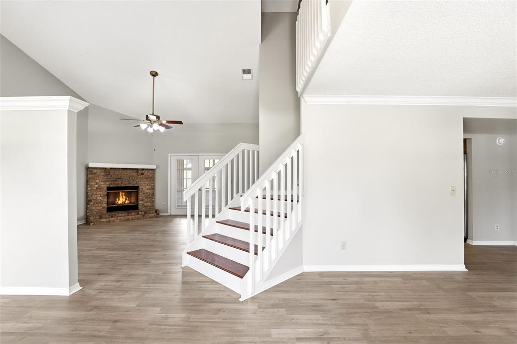 A living room with a brick fireplace, a staircase, and light wood-look flooring — 975 CROSS CUT WAY, LONGWOOD, FL