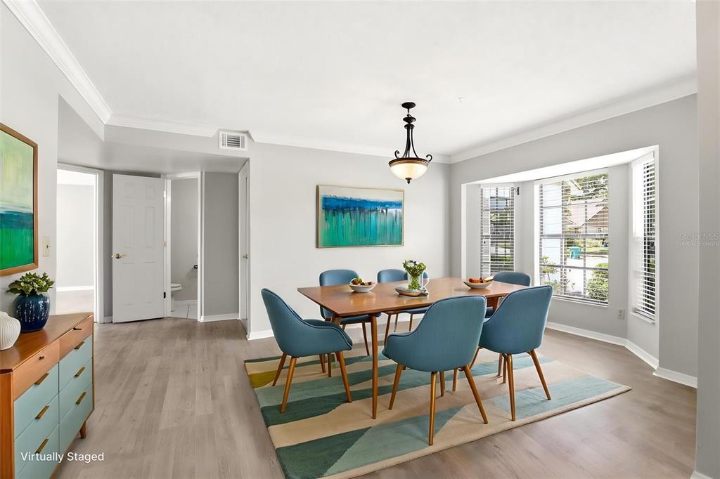 A dining room features a wooden table, blue chairs, a patterned rug, and bay windows — 975 CROSS CUT WAY, LONGWOOD, FL