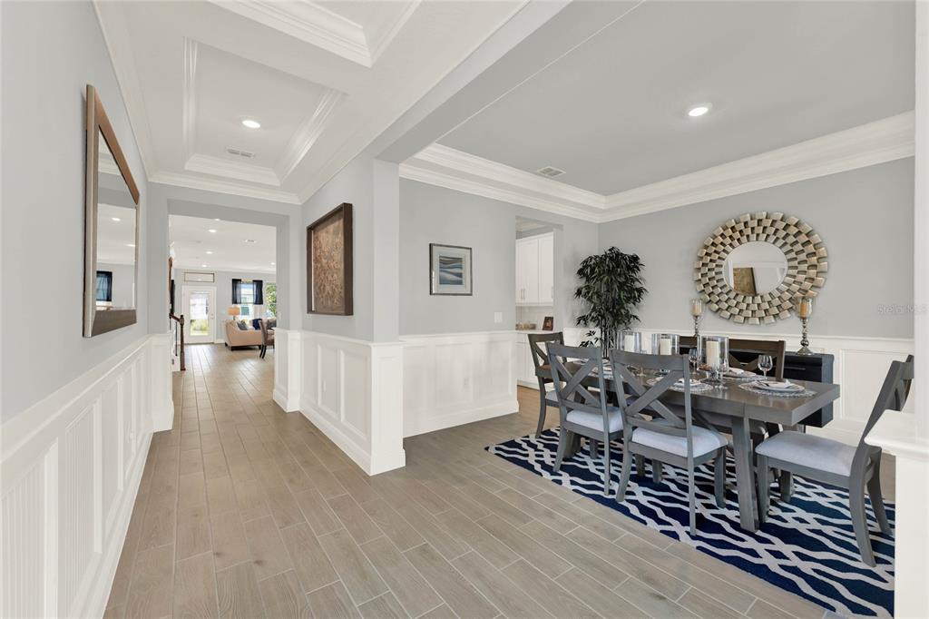 A dining room with a patterned rug, wooden table, and white wainscoting leads to a hallway — 11277 HOLLOW BAY DRIVE, WINTER GARDEN, FL