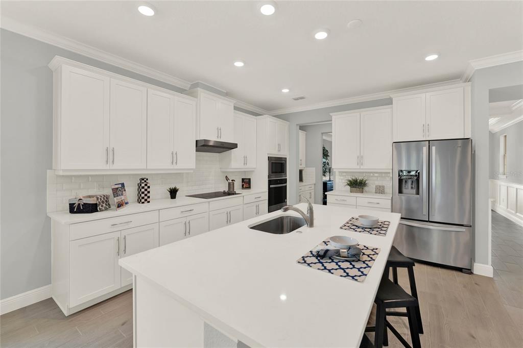 A modern kitchen features white cabinetry, a large central island with a sink, and stainless appliances — 11277 HOLLOW BAY DRIVE, WINTER GARDEN, FL