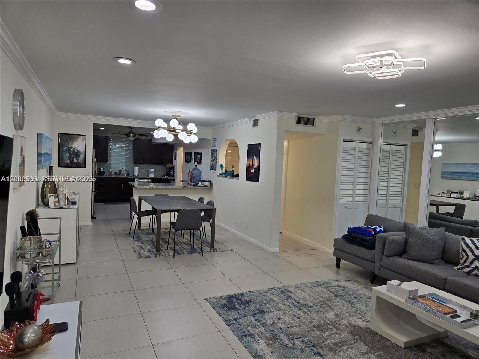 An open-concept living and dining area features tile flooring, a modern chandelier, and gray furniture — 295 Jacaranda Dr # 20, Plantation FL 33324, PLANTATION, FL