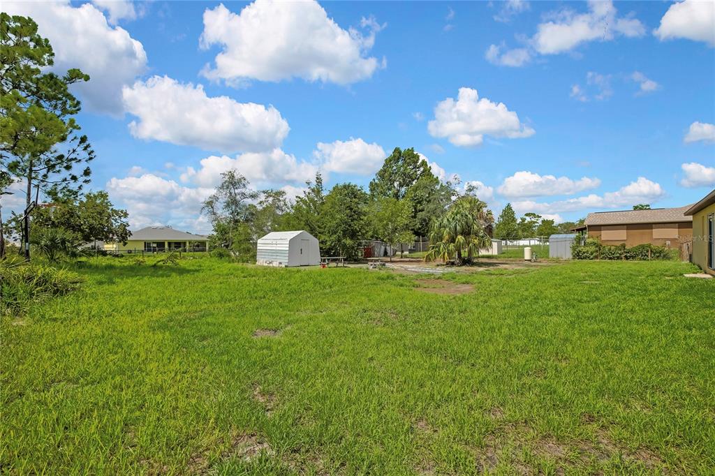 A grassy backyard features a white storage shed, scattered trees, and neighboring houses — 13134 OSPREY AVENUE, WEEKI WACHEE, FL