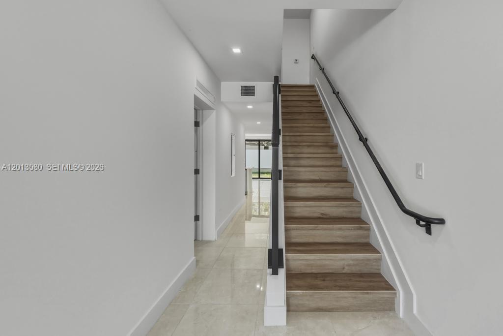A staircase with wood treads and a black handrail leads upward in a white hallway — 4120 S Oak Pl, Dania Beach FL 33314, DANIA BEACH, FL