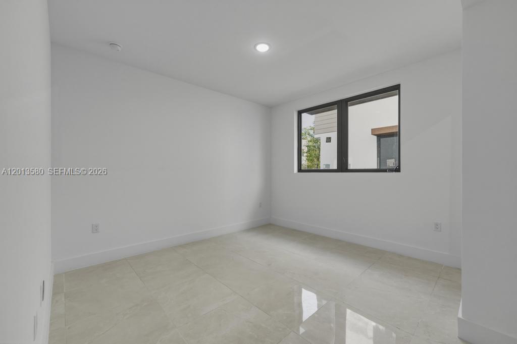 A minimalist bedroom features white walls, light tile flooring, and a large black-framed window — 4120 S Oak Pl, Dania Beach FL 33314, DANIA BEACH, FL
