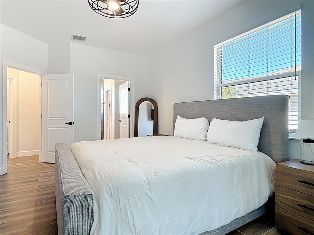 A bedroom features a gray upholstered bed, light wood flooring, and a large window — 26 MEDALIST WAY, ROTONDA WEST, FL