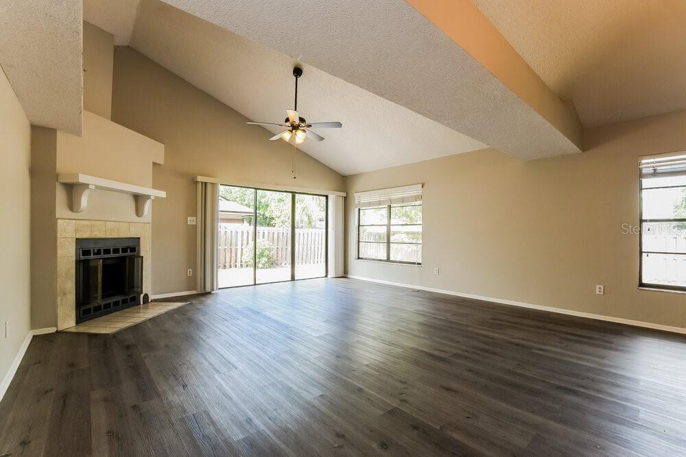 An empty living room features a vaulted ceiling, a fireplace, and wood-look flooring — 3598 S SAINT LUCIE DRIVE, CASSELBERRY, FL
