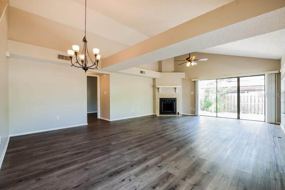 A spacious living room features dark wood-look flooring, a vaulted ceiling, and a corner fireplace — 3598 S SAINT LUCIE DRIVE, CASSELBERRY, FL