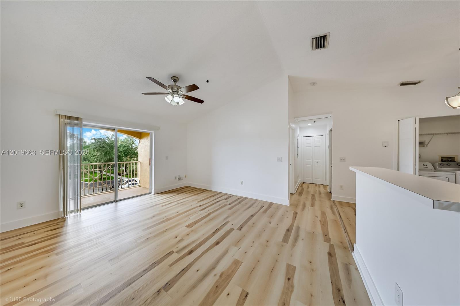 An empty living room features light wood-look flooring, a ceiling fan, and a sliding glass door — 5570 NW 61st St # 930, Coconut Creek FL 33073, COCONUT CREEK, FL
