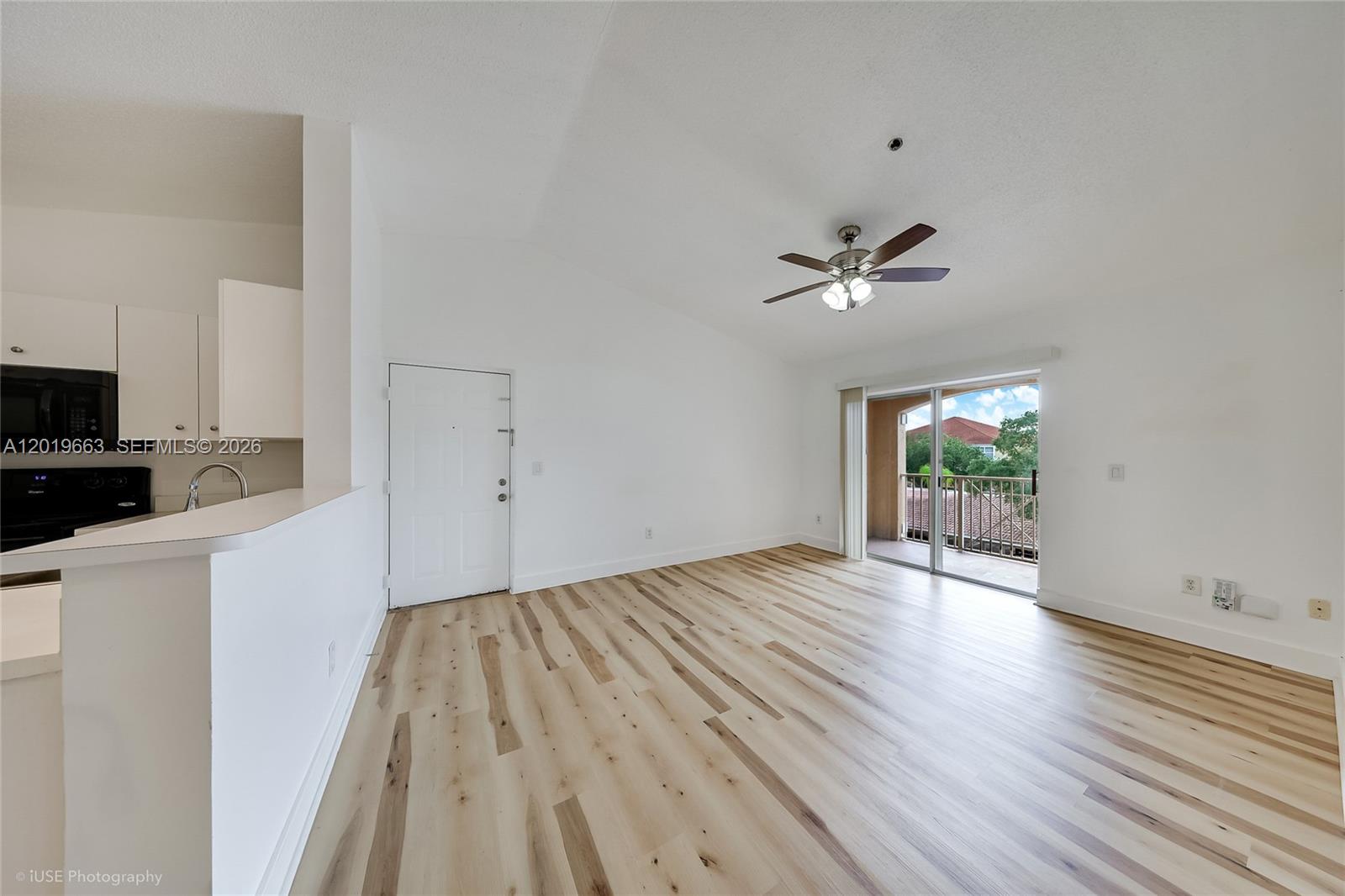 An empty living room with light wood flooring, a ceiling fan, and a sliding glass door — 5570 NW 61st St # 930, Coconut Creek FL 33073, COCONUT CREEK, FL