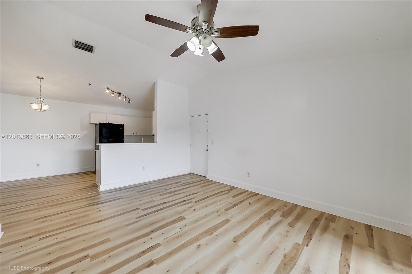 This living room features wood-look flooring, a ceiling fan, and an adjacent kitchen area — 5570 NW 61st St # 930, Coconut Creek FL 33073, COCONUT CREEK, FL