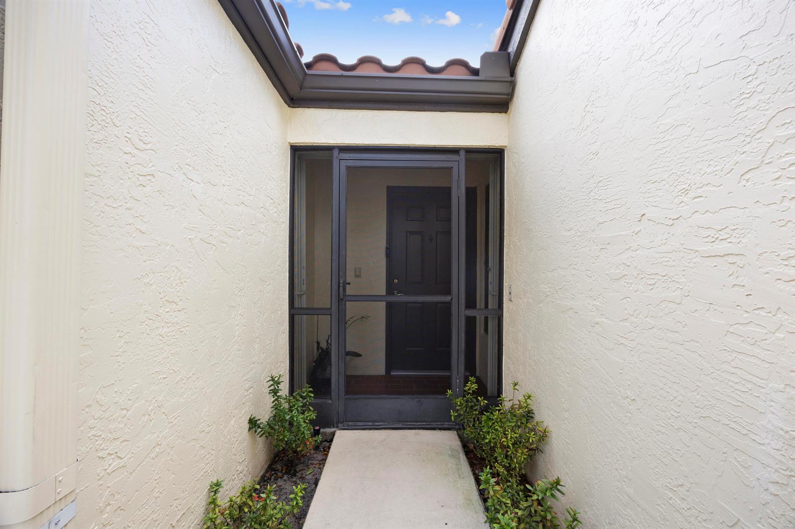 A concrete walkway leads to a dark front door enclosed by a screened entryway — 5916 Sunswept Lane # A, Boynton Beach FL 33437, BOYNTON BEACH, FL