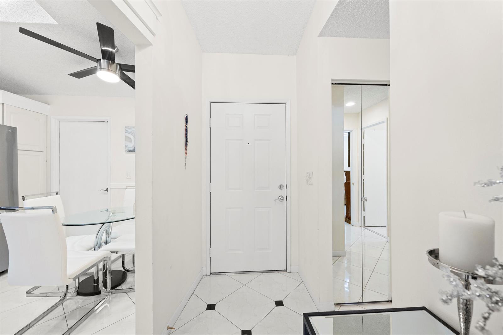 A white entryway features tiled floors with black accents, a front door, and mirrored closet doors — 5916 Sunswept Lane # A, Boynton Beach FL 33437, BOYNTON BEACH, FL