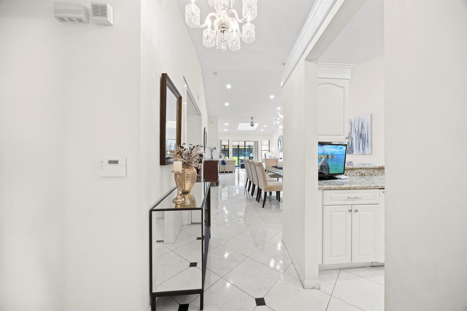 A bright entryway with a crystal chandelier leads into a dining area with tiled floors — 5916 Sunswept Lane # A, Boynton Beach FL 33437, BOYNTON BEACH, FL