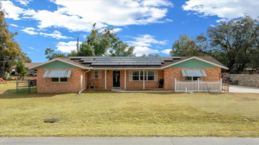 A single-story brick house with a solar panel roof and a white picket fence — 10629 SE 51ST AVENUE, BELLEVIEW, FL