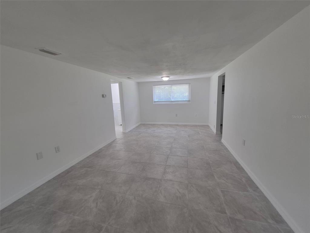 An empty room features white walls, a gray tiled floor, and a single window — 27 E LEMON STREET, BEVERLY HILLS, FL