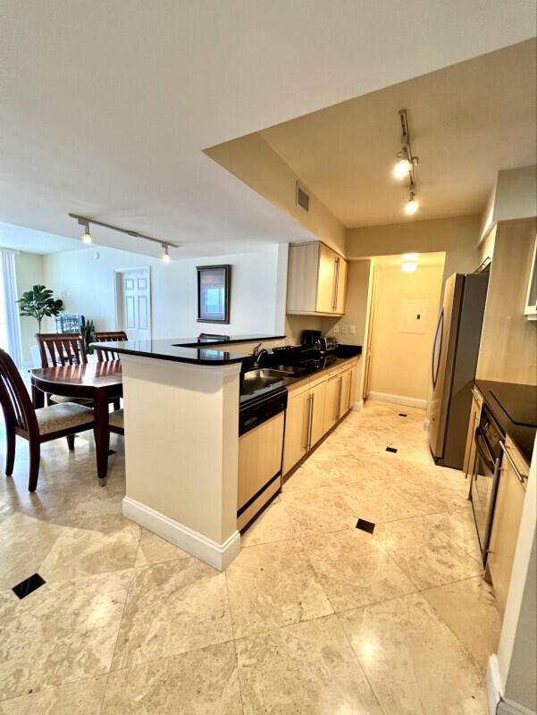 A kitchen with light wood cabinets, black countertops, and tile flooring opens to a dining area — 2080 S Ocean Drive # 1608, Hallandale Beach FL 33009, HALLANDALE BEACH, FL