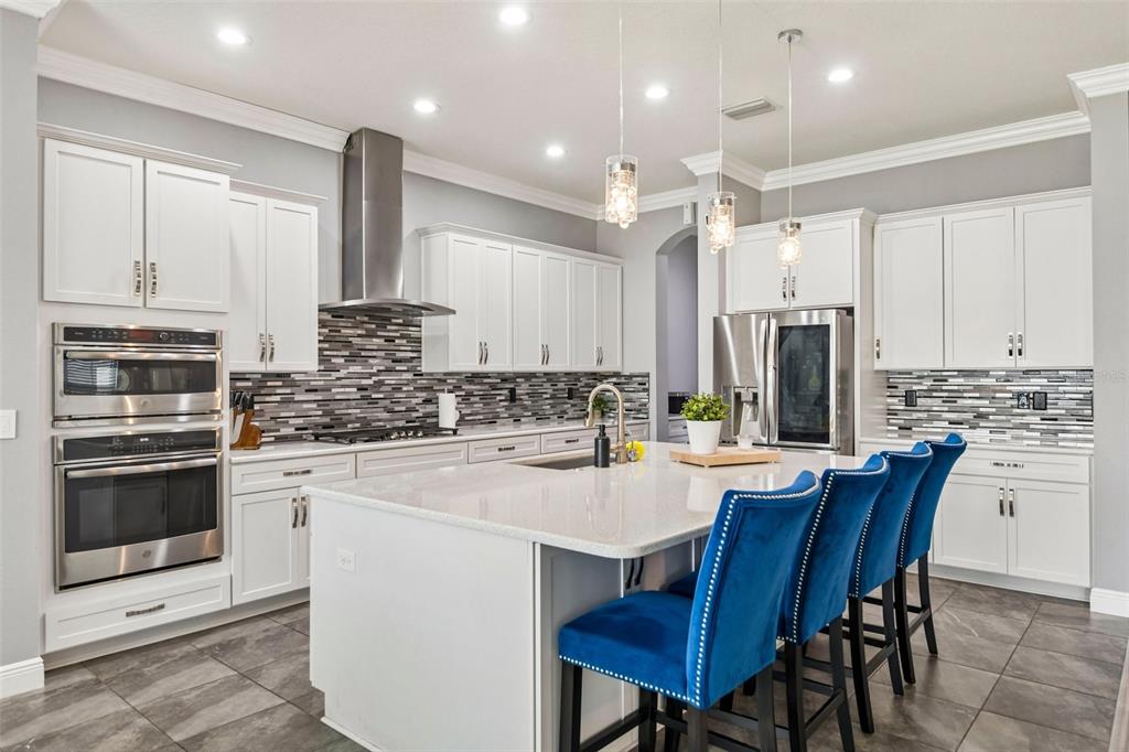A modern kitchen features white cabinets, stainless steel appliances, a tiled backsplash, and a central island — 19529 HAYDEN LAKE COURT, LAND O LAKES, FL