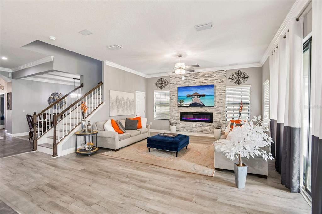 A living room features a stone fireplace, a wall-mounted television, and a staircase — 19529 HAYDEN LAKE COURT, LAND O LAKES, FL