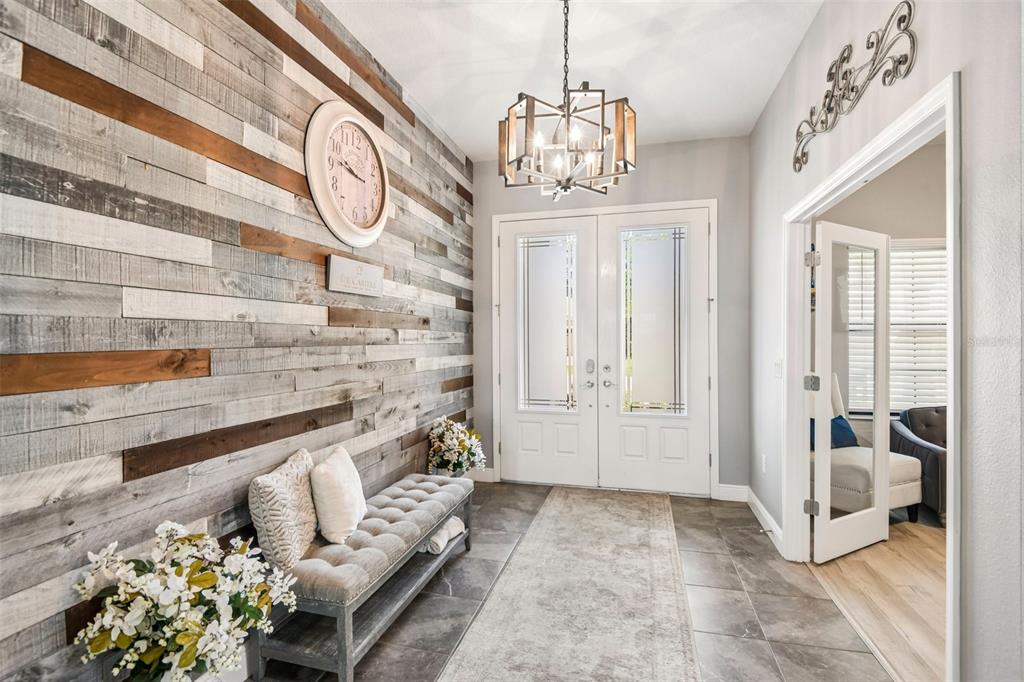 An entryway features a wood-plank accent wall, a tufted bench, and a modern chandelier — 19529 HAYDEN LAKE COURT, LAND O LAKES, FL