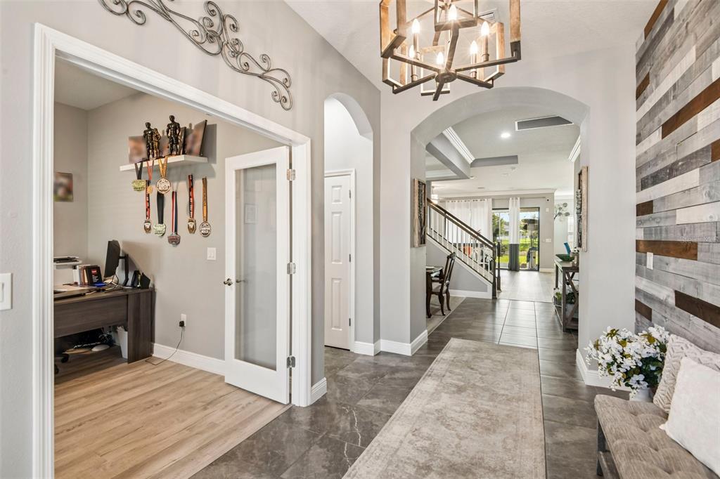 A home entryway features a wood-paneled wall, a chandelier, and a glass-paneled office door — 19529 HAYDEN LAKE COURT, LAND O LAKES, FL
