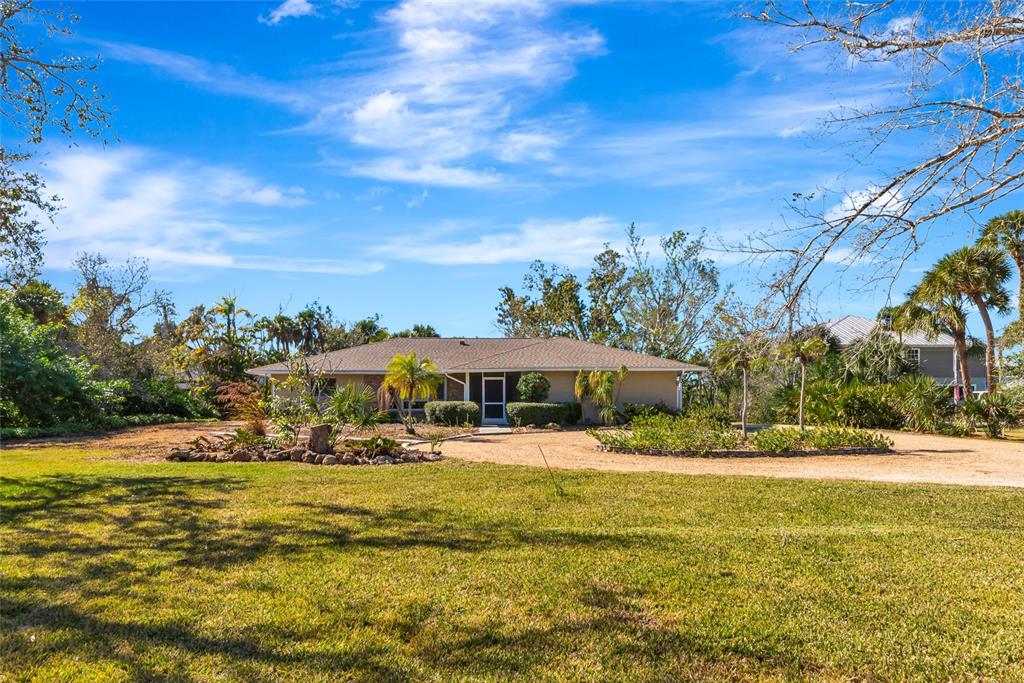 A single-story house with a gravel driveway sits on a grassy lot with palm trees — 950 OXFORD DRIVE, ENGLEWOOD, FL