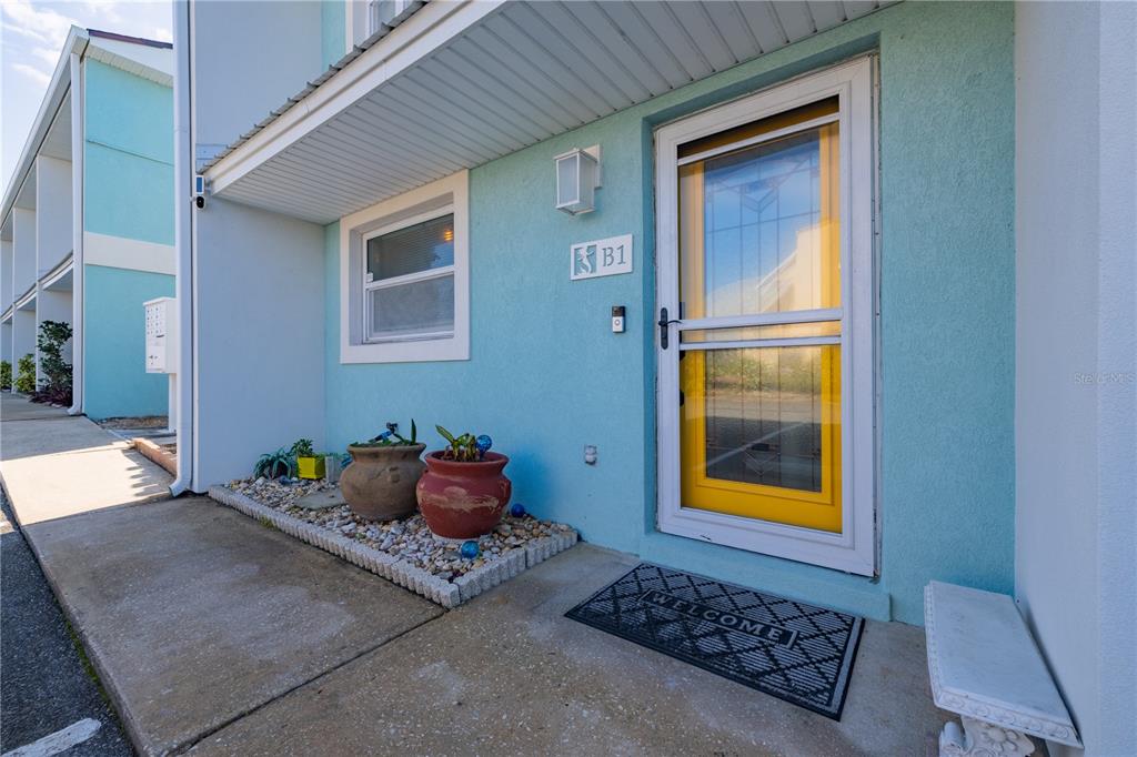 The exterior of a light blue building features a yellow front door labeled B1 — 4786 S ATLANTIC AVENUE UNIT B1, PONCE INLET, FL