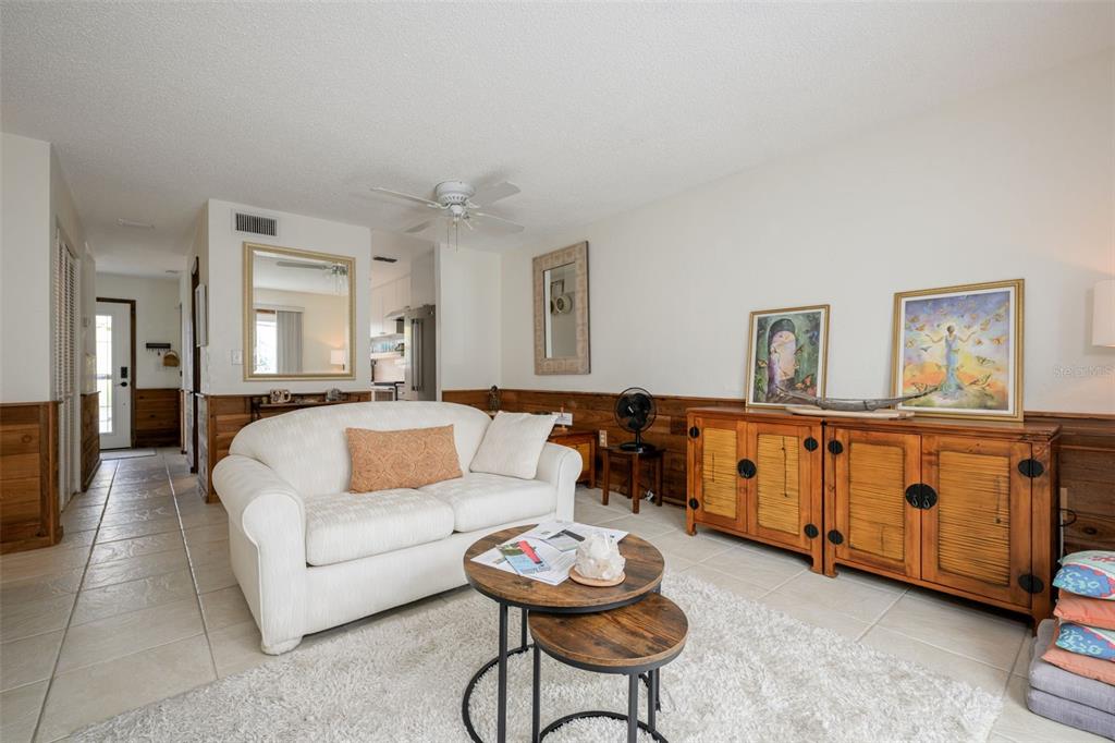 A living room features a sliding glass door, wood wainscoting, tile flooring, and two sofas — 4786 S ATLANTIC AVENUE UNIT B1, PONCE INLET, FL