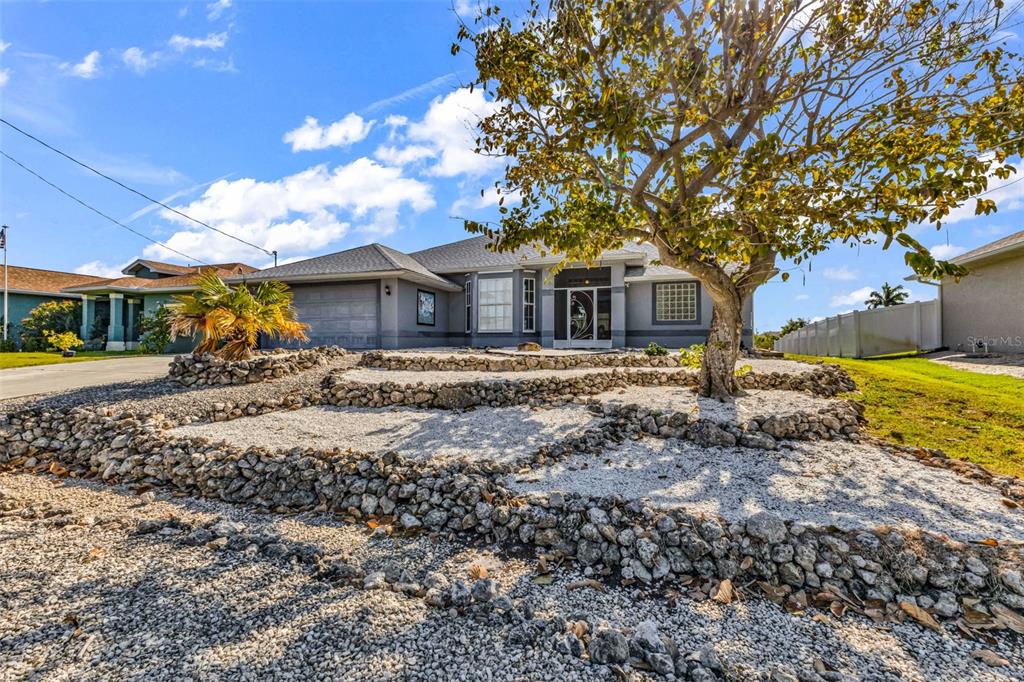 A single-story gray house features a terraced rock garden and a large tree in front — 9582 ARSIPE CIRCLE, PORT CHARLOTTE, FL